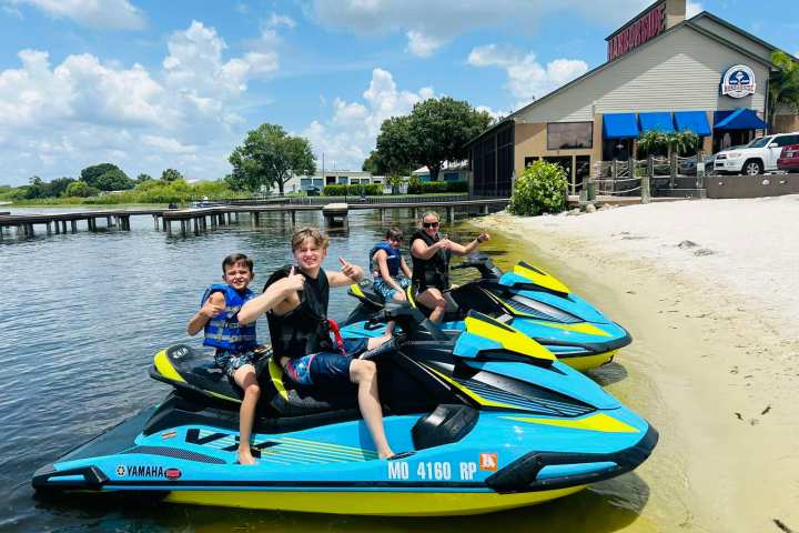 Three people on jet skis by a restaurant on a sunny day.