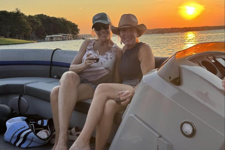 Two people on a boat at sunset, enjoying drinks and smiling.