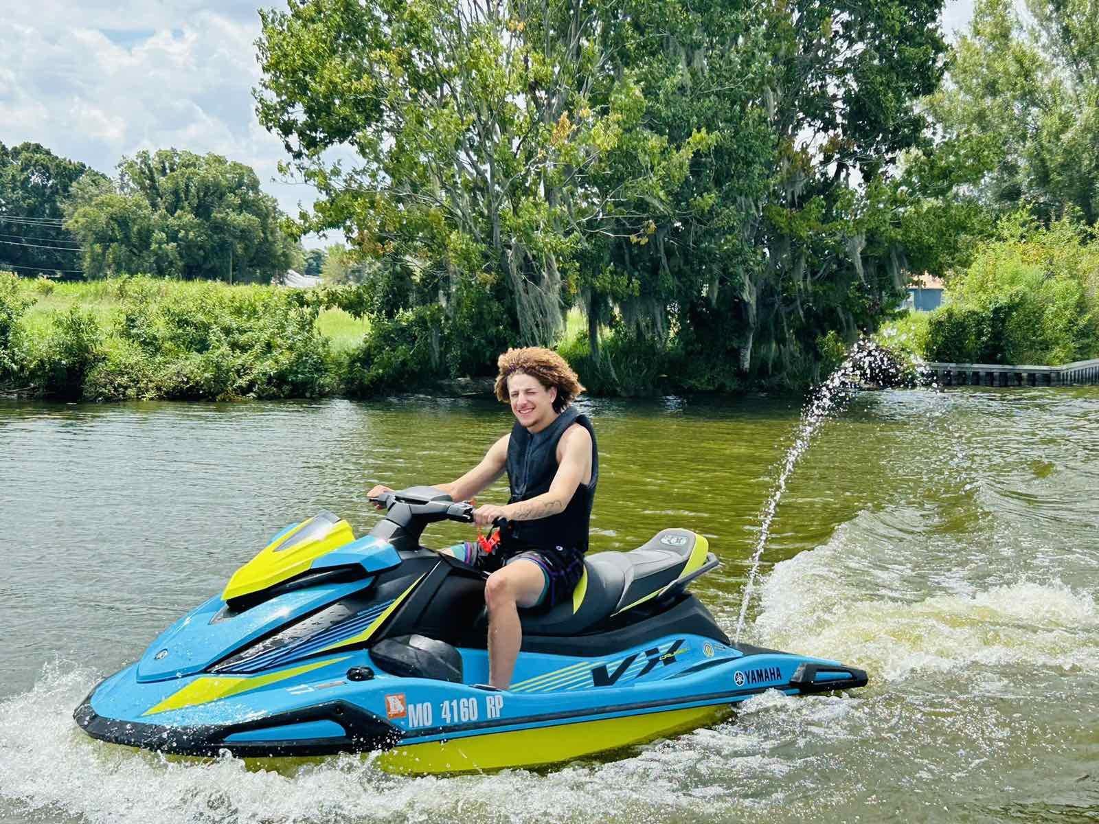 Person riding a blue and yellow jet ski on a calm river on a sunny day.