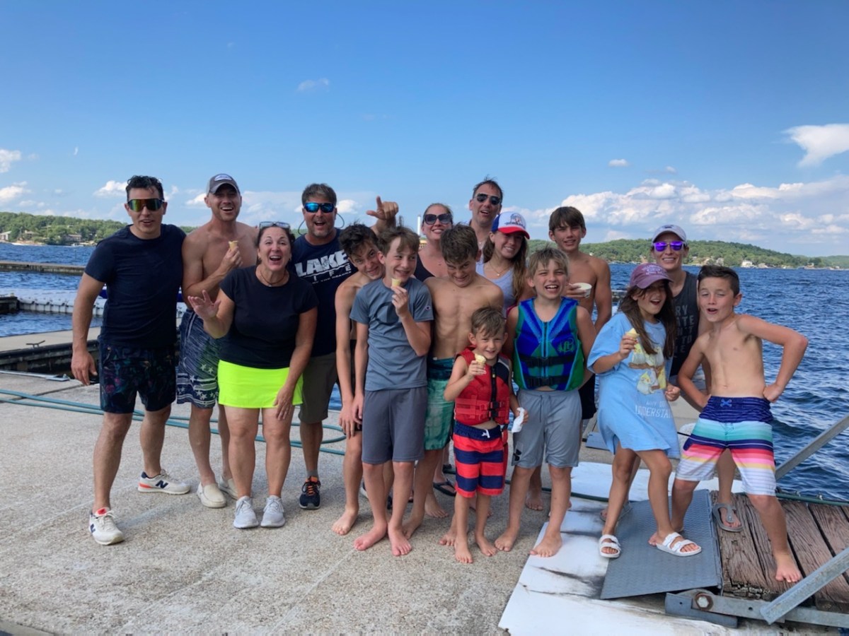 Group of people smiling on a dock by a lake, with blue sky in the background.