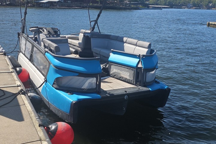 Blue and black boat docked on a sunny lake with buoys and seating.