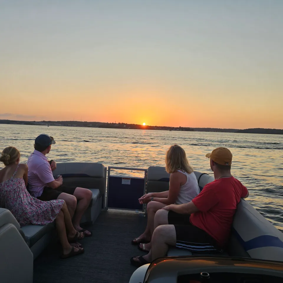 Four people on a boat watch the sunset over a calm lake.