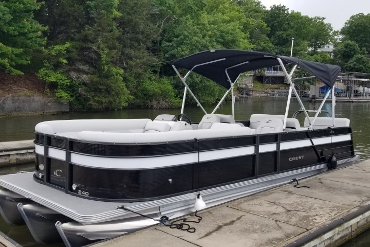 Pontoon boat docked on a lake with a canopy and greenery in the background.